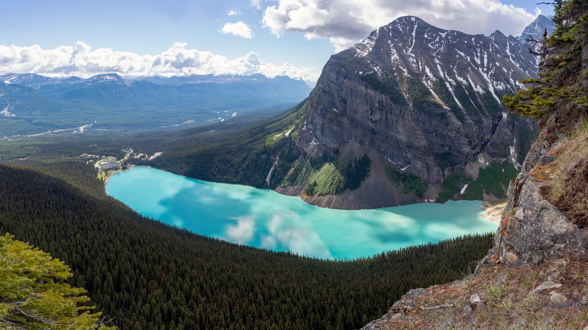 Turquoise Lake Louise and its lodge seen from above beneath a steep mountain face